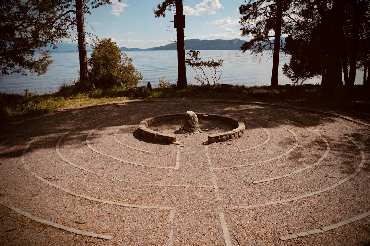 A stone labyrinth near a lake with trees and mountains.
